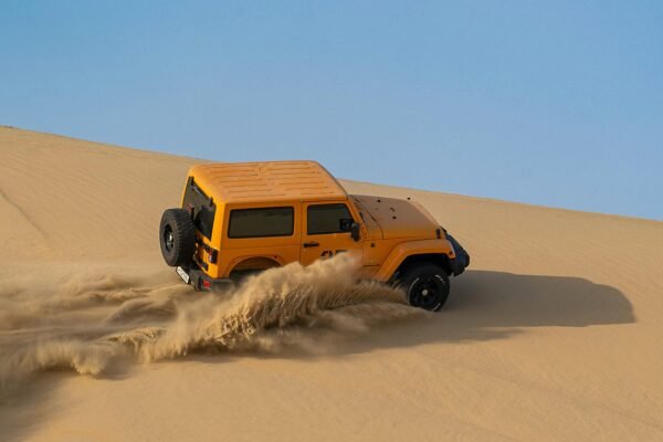 Yellow 4x4 with a spare wheel on the rear door climbing a steep Namib dune, throwing up a wall of sand